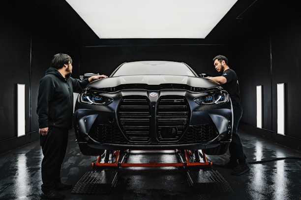 a couple of men standing next to a car in a garage
