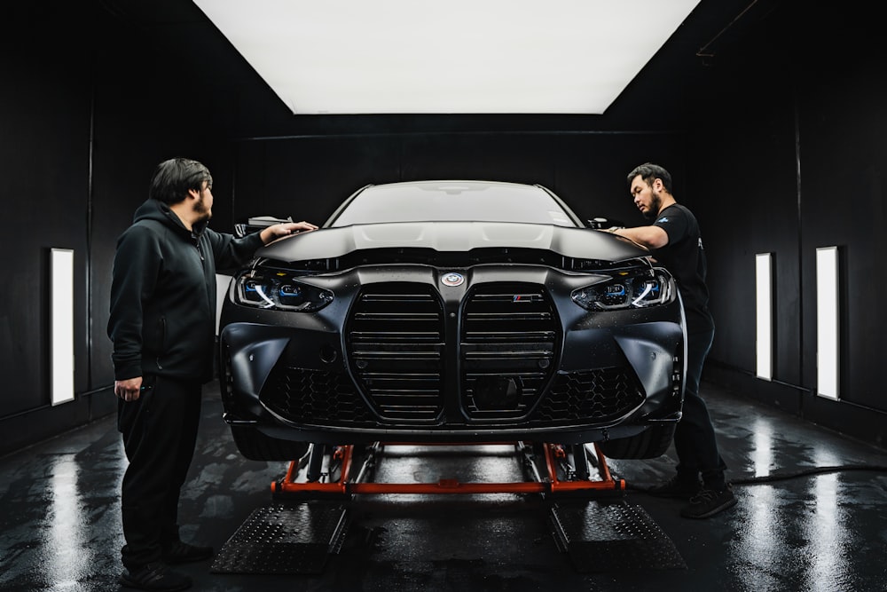 a couple of men standing next to a car in a garage