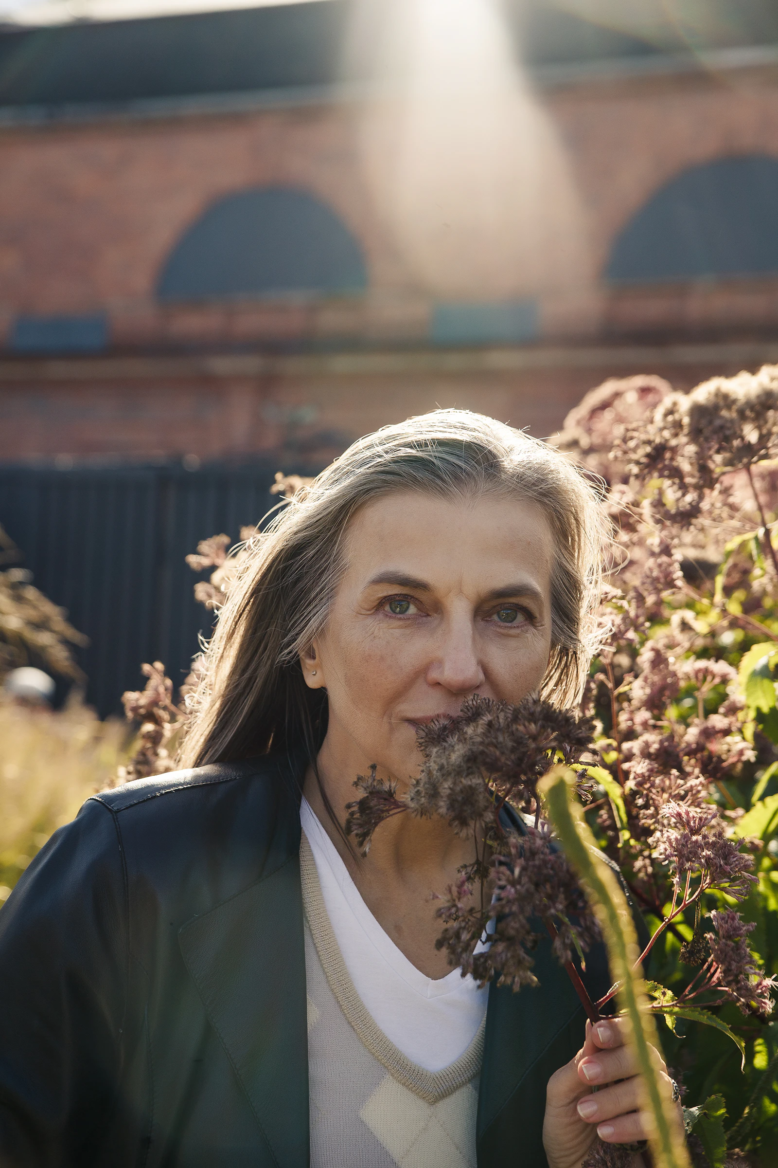 Femme d'âge mûr sereine, cheveux gris, souriante en extérieur parmi des fleurs