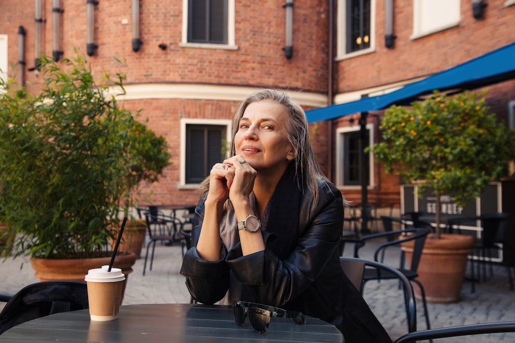 Woman alone at an outdoor cafe table, contemplative, brick building behind her