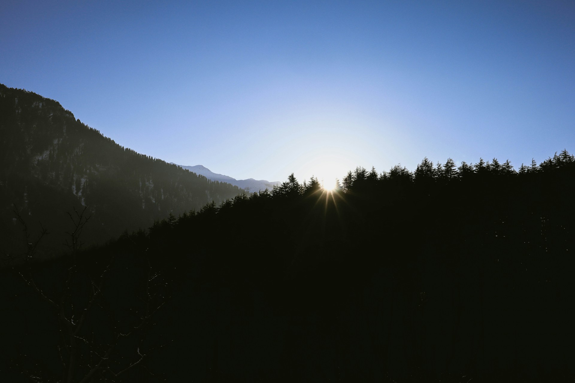 A serene sunrise over Chopta meadows with the silhouette of Tungnath temple nestled among lush green hills.