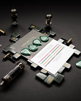 Green guitar picks are arranged on a printed card with technical information about their dimensions. The layout is set on a black surface, surrounded by circuit-related components and industrial elements. The overall aesthetic combines musical accessories with an industrial design theme.