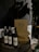 Wine bottles are placed on a wooden barrel next to stacked pizza boxes with the label 'Pizza Locale.' The setting includes a dimly lit ambiance with a potted plant nearby and a tiled wall in the background.
