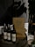 Wine bottles are placed on a wooden barrel next to stacked pizza boxes with the label 'Pizza Locale.' The setting includes a dimly lit ambiance with a potted plant nearby and a tiled wall in the background.