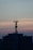 A telecommunications tower is perched on top of a high-rise building against a backdrop of a dusky sky. The sky is painted with gradients of blue and orange, reflecting the transition from day to night.