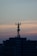 A telecommunications tower is perched on top of a high-rise building against a backdrop of a dusky sky. The sky is painted with gradients of blue and orange, reflecting the transition from day to night.