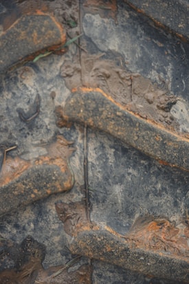 Close-up view of a large, muddy tire with thick, rugged treads embedded with dirt.