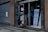Two children are outside a building entrance with a sign indicating a kids' sale event scheduled for October 31, 2022. The building has a large, closed metal shutter, and the children are engaged in conversation or observation.