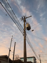 Technician hands installing electrical cables on a wooden utility pole at sunset.