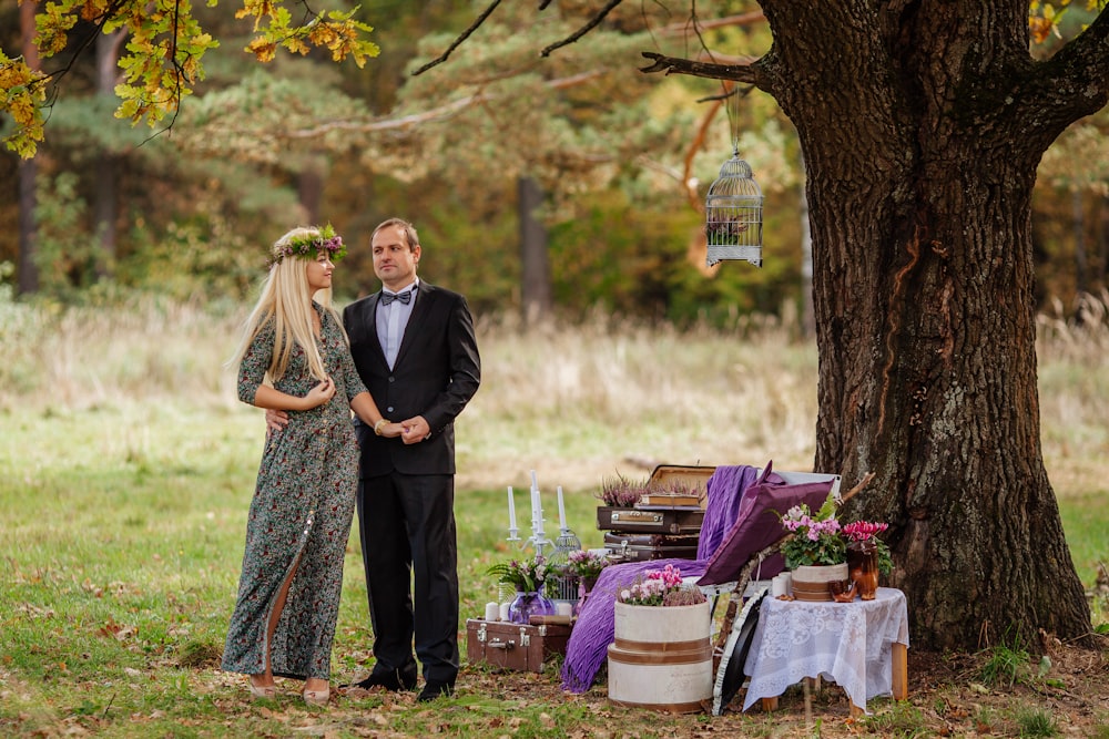 a man and woman standing next to a tree and a table with flowers