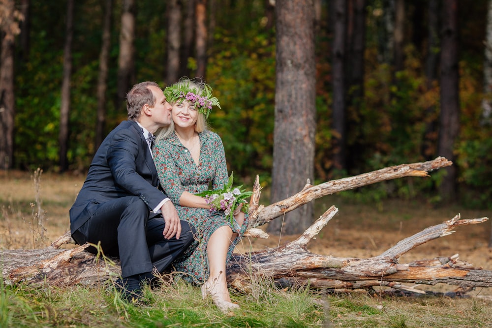 a man and woman sitting on a log in the woods