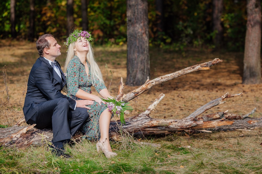 a man and woman sitting on a log in the woods