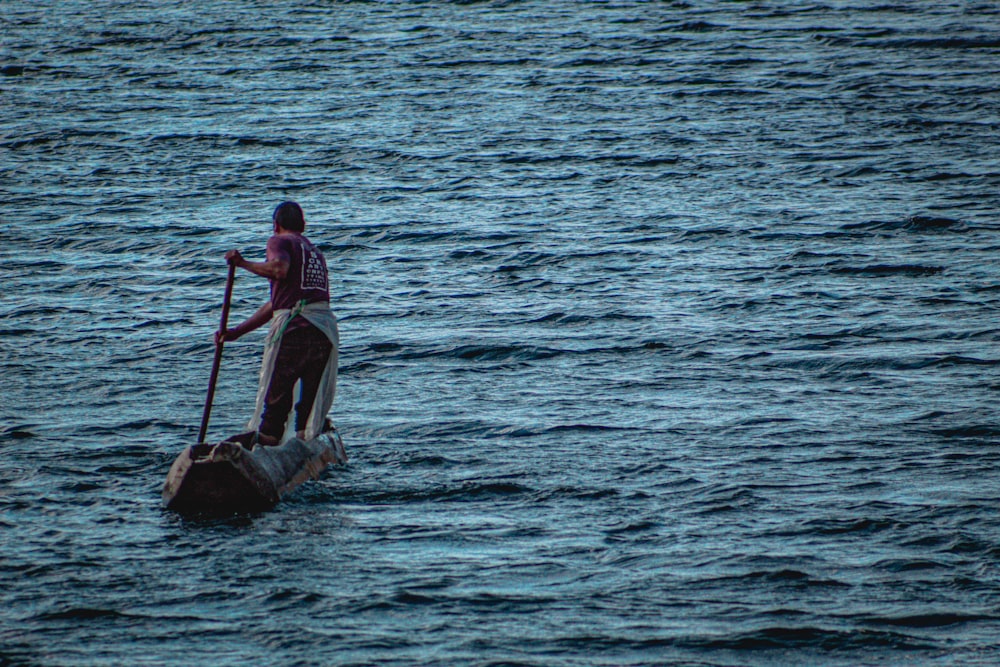 a man on a surfboard holding a paddle while standing on a rock in the water