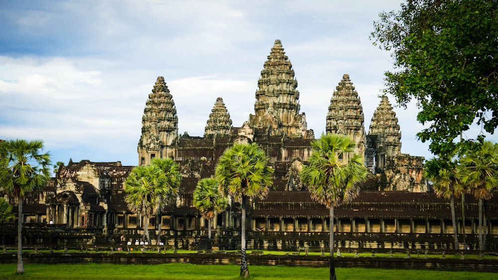 a large building with towers and palm trees with Angkor Wat in the background