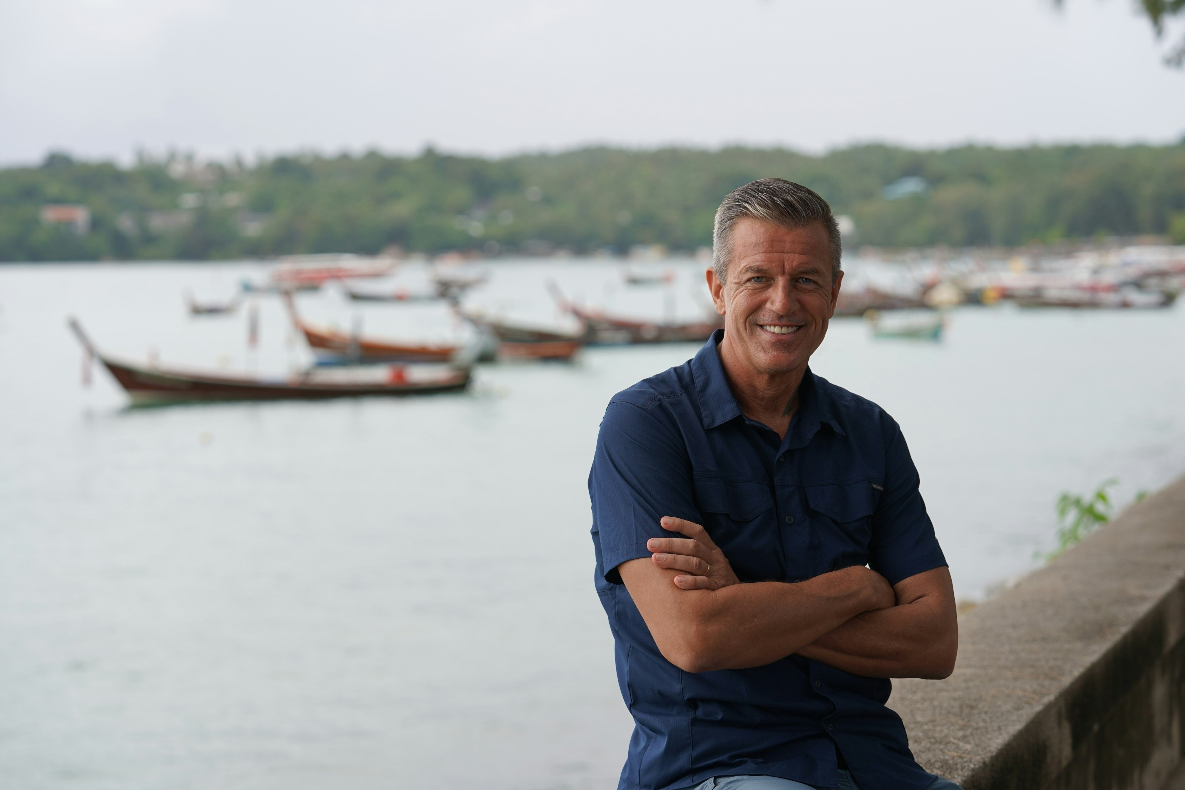 a man leaning on a wall with a body of water behind him