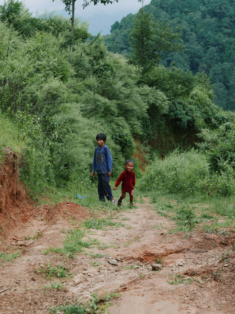 a man and a boy walking on a dirt path in the woods