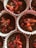 Several chocolate cupcake batter portions are placed in white and pink paper liners, topped with slices of strawberries, pink wafer pieces, and chocolate shavings.
