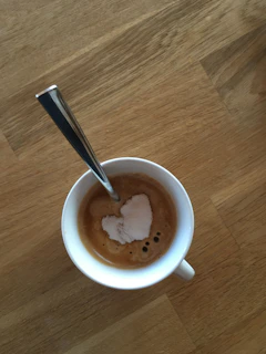 An overhead shot of a coffee cup with a heart-shaped foam design, resting on a rustic wooden table.