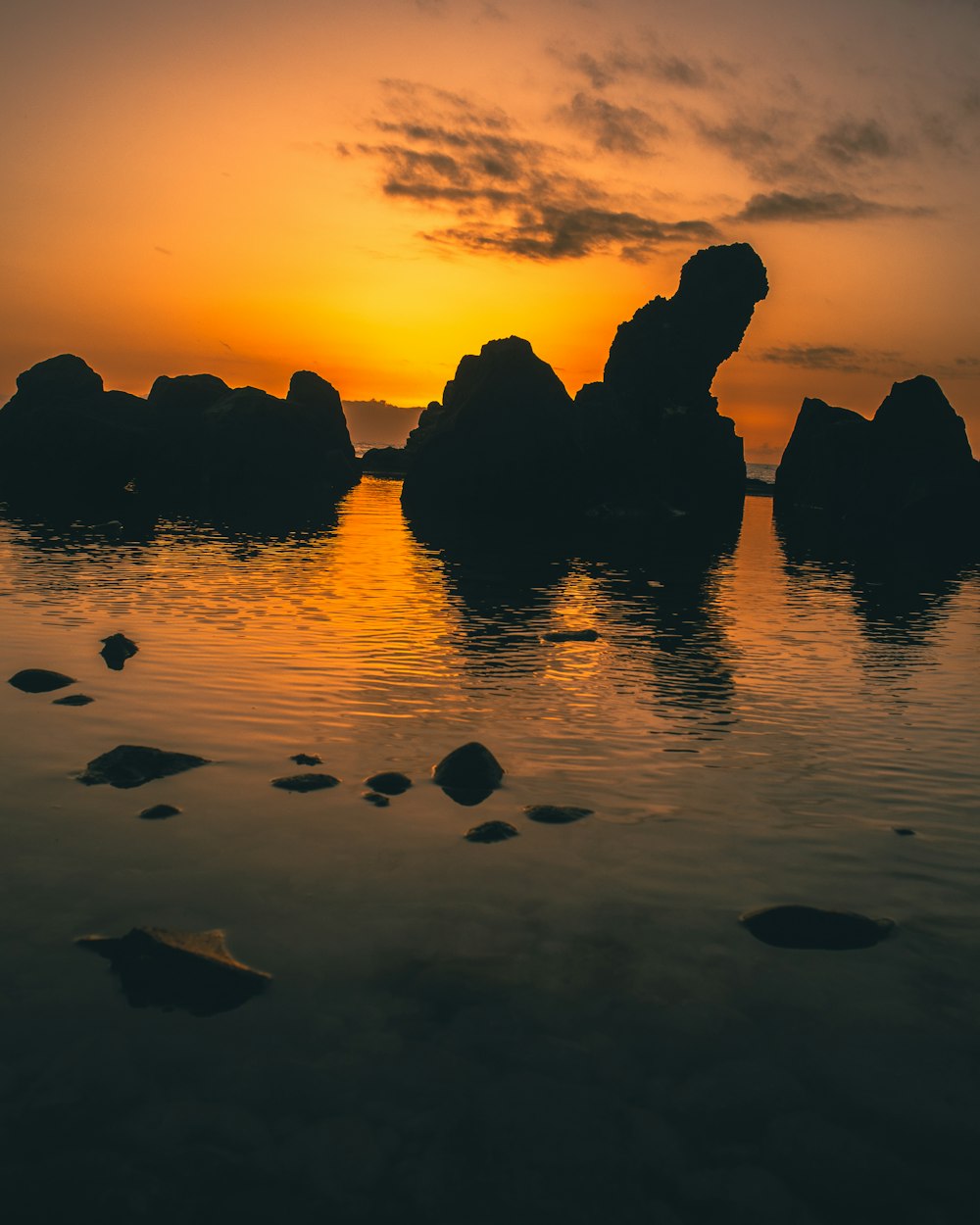 a body of water with rocks and a sunset in the background