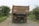 A heavily loaded truck is seen on a narrow rural road surrounded by greenery. The back of the truck features colorful decorations including stars and the word 'STOP'. The road is unpaved and appears dusty.