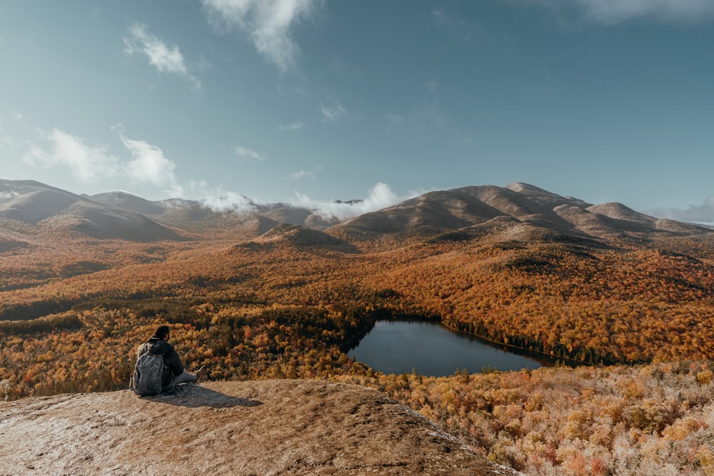 Una persona sentada en una roca mirando un lago rodeado de montañas