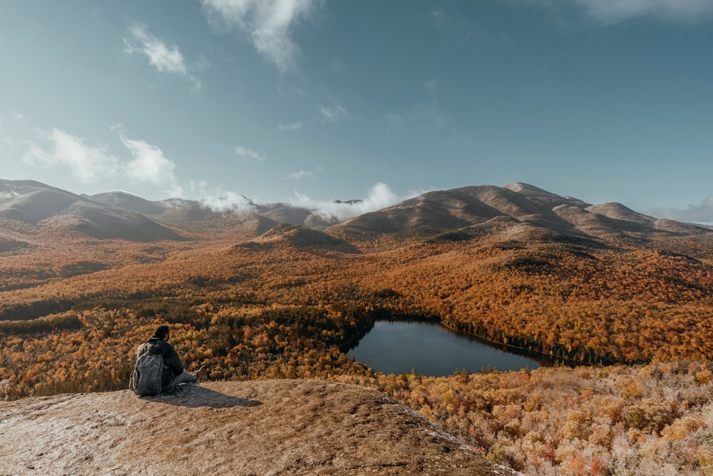 a person sitting on a rock looking at a lake surrounded by mountains