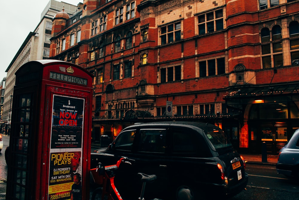 a black car parked next to a red telephone booth