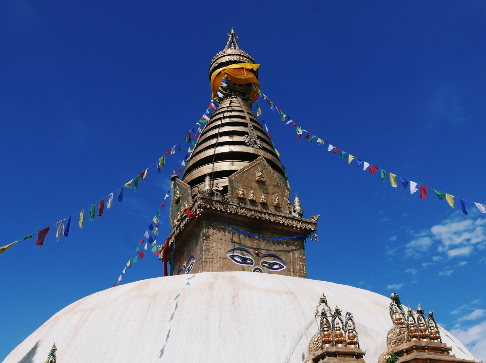 The painted eyes of the Buddha on Swayambhunath's gilded tower, prayer flags running out against a deep blue sky