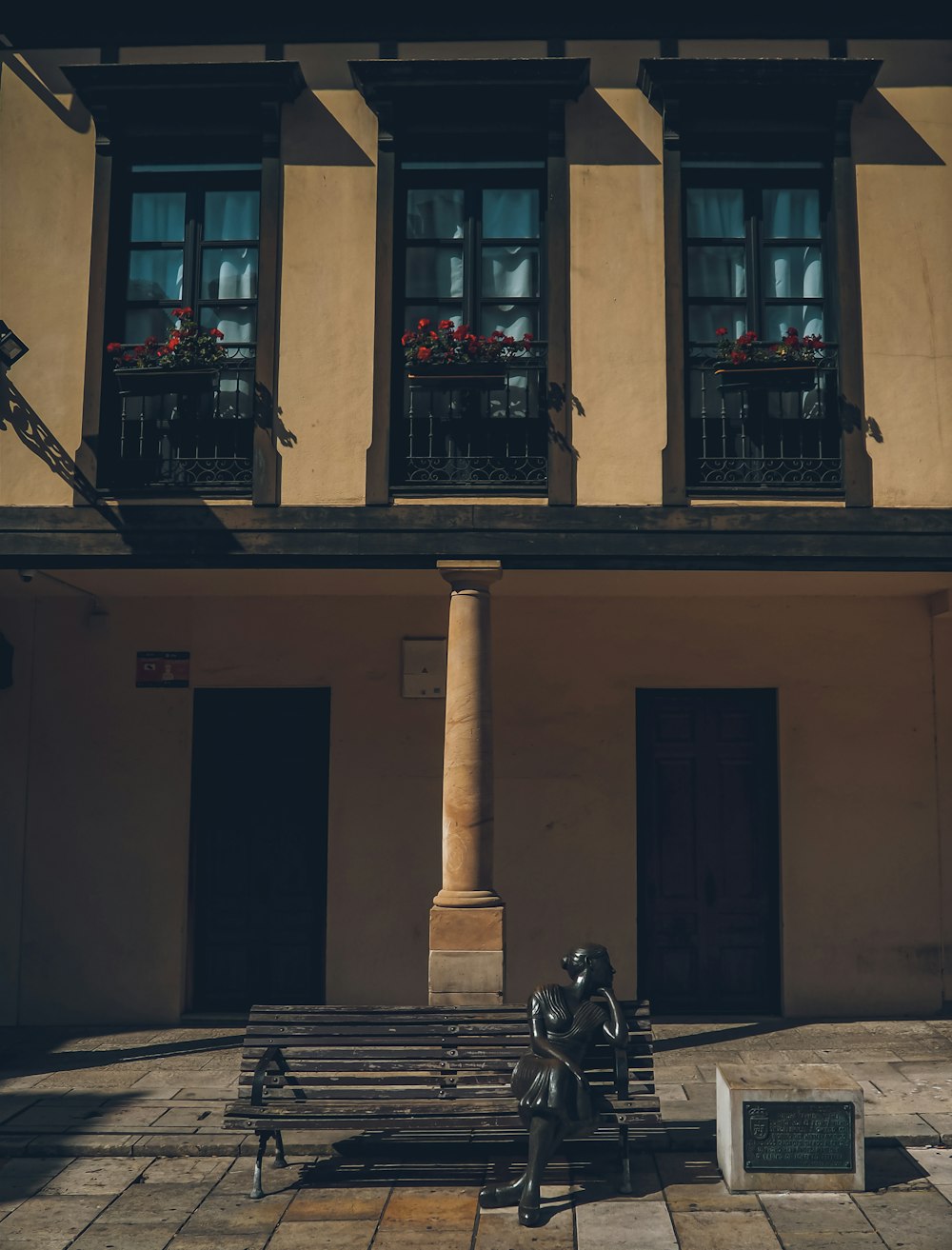 une statue d’une personne assise sur un banc devant un bâtiment