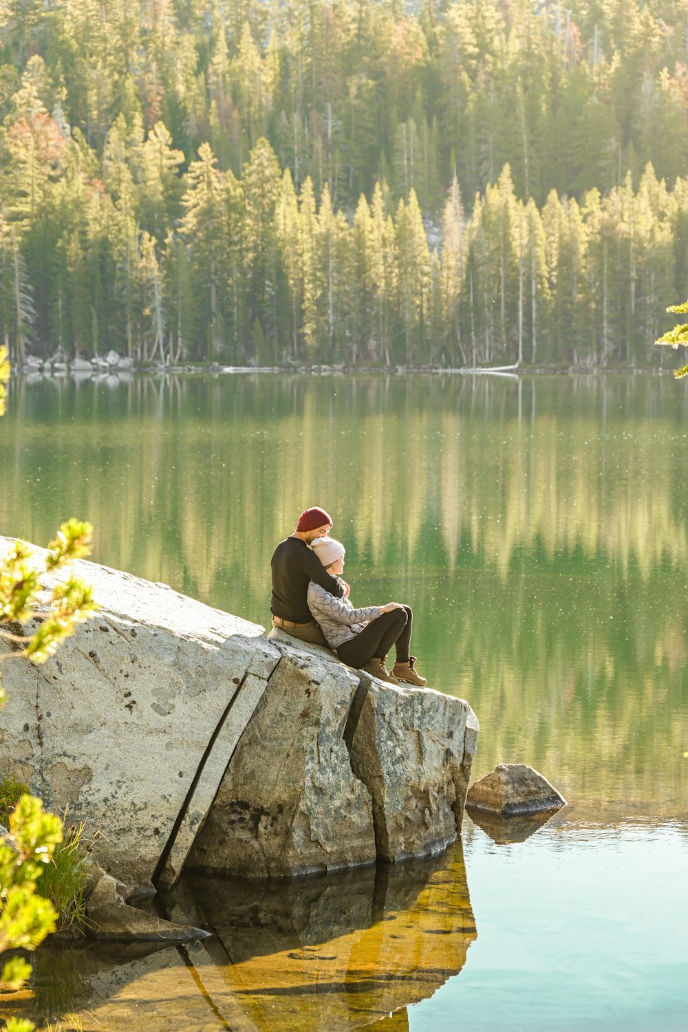 a person sitting on a rock by a lake with trees in the background