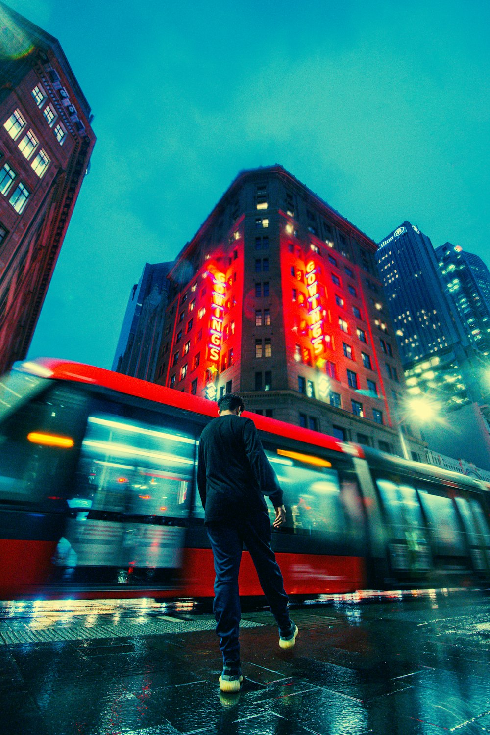 a person walking on a sidewalk in front of a bus and buildings