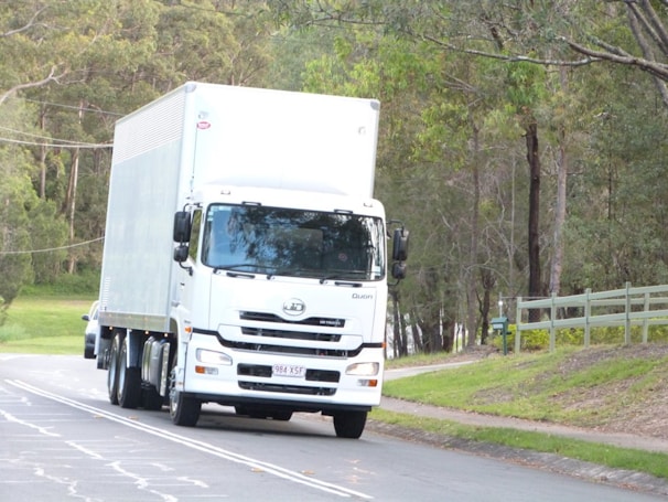 Wide shot of a transport truck driving along a highway surrounded by green fields.