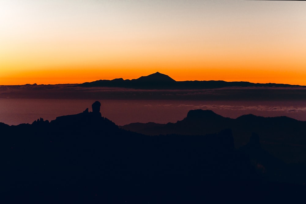 Eine Person, die auf einem Felsen sitzt und den Sonnenuntergang betrachtet