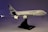 A model airplane of the Airbus A380 is displayed on a black stand. The aircraft is white with blue accents, featuring detailed engines and landing gear. The lighting casts a gradient of purple hues in the background.