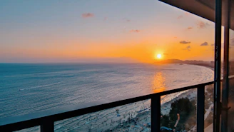 Sunset over the ocean viewed from a spacious balcony with elegant coastal furnishings.