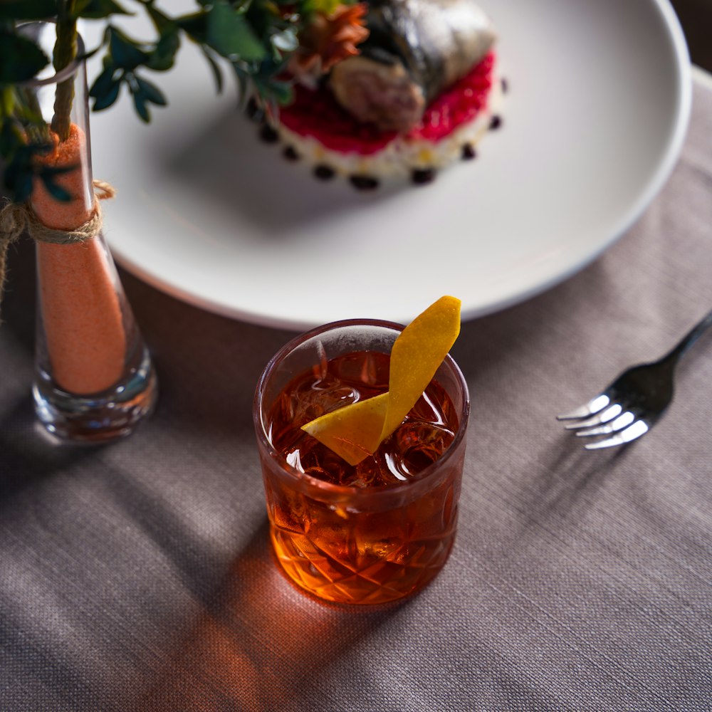 a glass of orange juice with a slice of orange on a plate