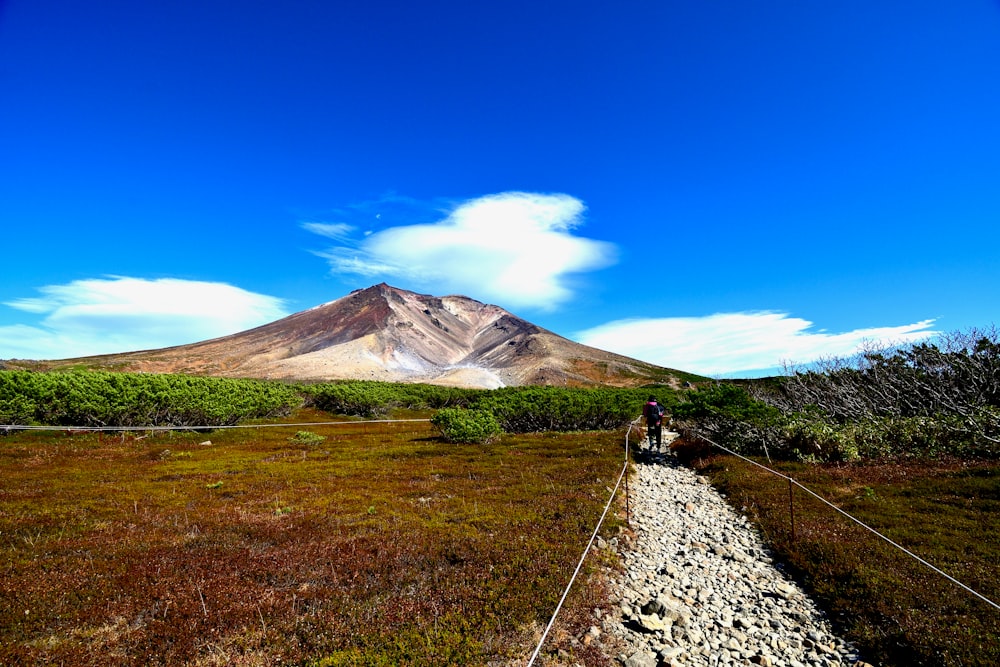 a person riding a bicycle on a dirt road with a mountain in the background