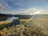 A sturdy tent pitched beside a serene mountain lake at sunset