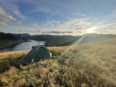 A sturdy olive-green military tent pitched beside a calm Scandinavian lake at dawn.