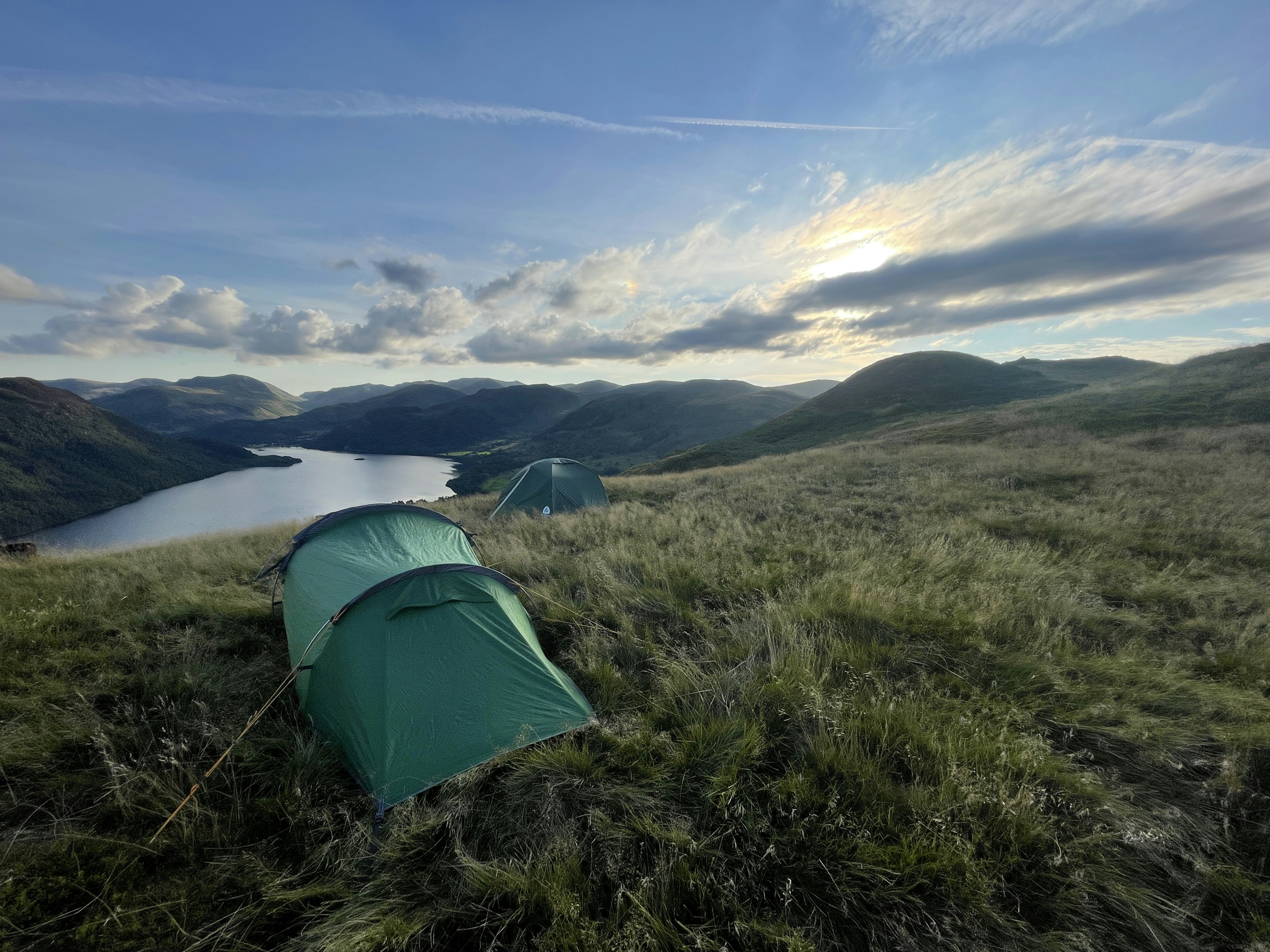 a couple of tents in a grassy field by a lake