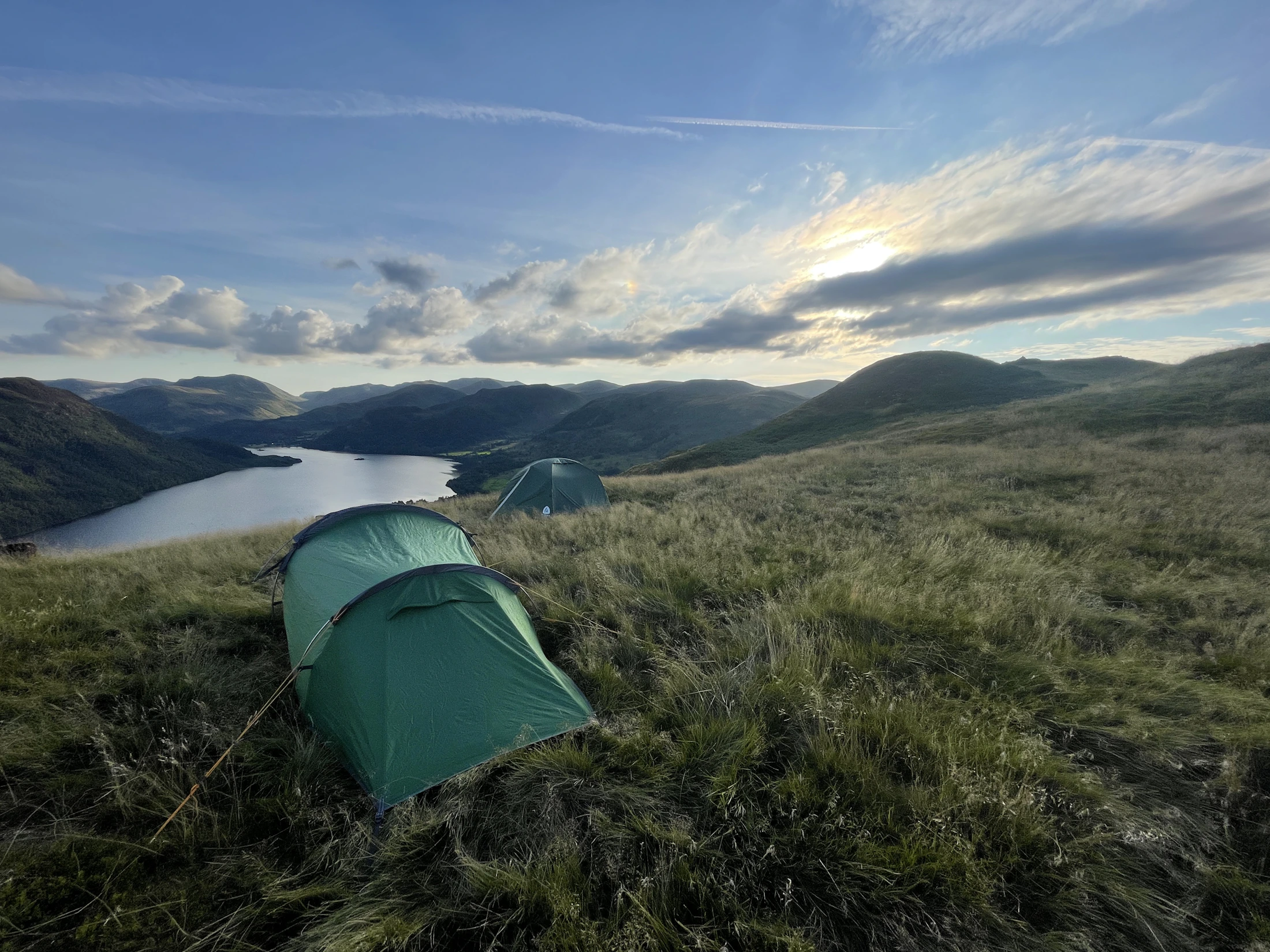 Two green camping tents overlooking a lake and mountain landscape