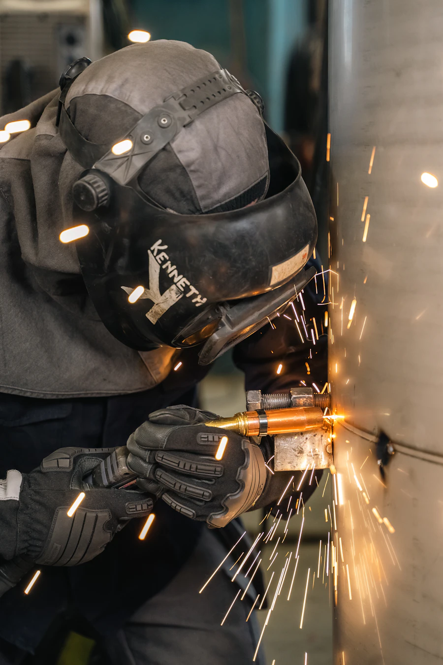 Welder in a hood laying a bead on steel plate inside a training booth