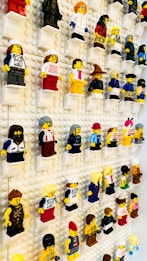 A display of multiple LEGO minifigures mounted on a white pegboard. Each figure is positioned on its own small platform and showcases a variety of colorful outfits and accessories.