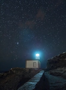 a house on a rocky shore at night with the milky way above