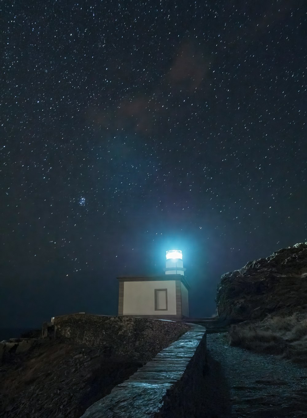 a house on a rocky shore at night with the milky way above