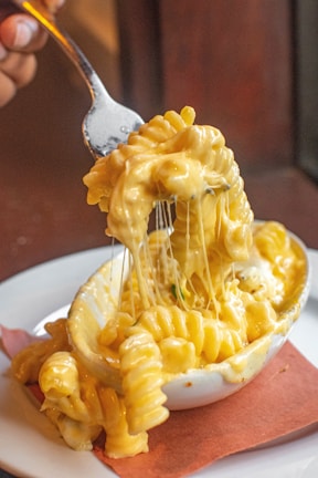 A spoon lifting cheesy beef and noodles from the casserole, showing gooey melted cheese.