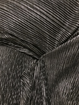 A close-up of metallic ribbed fabric showcasing fine parallel lines with a glossy texture, the surface catches light creating highlights and shadows.