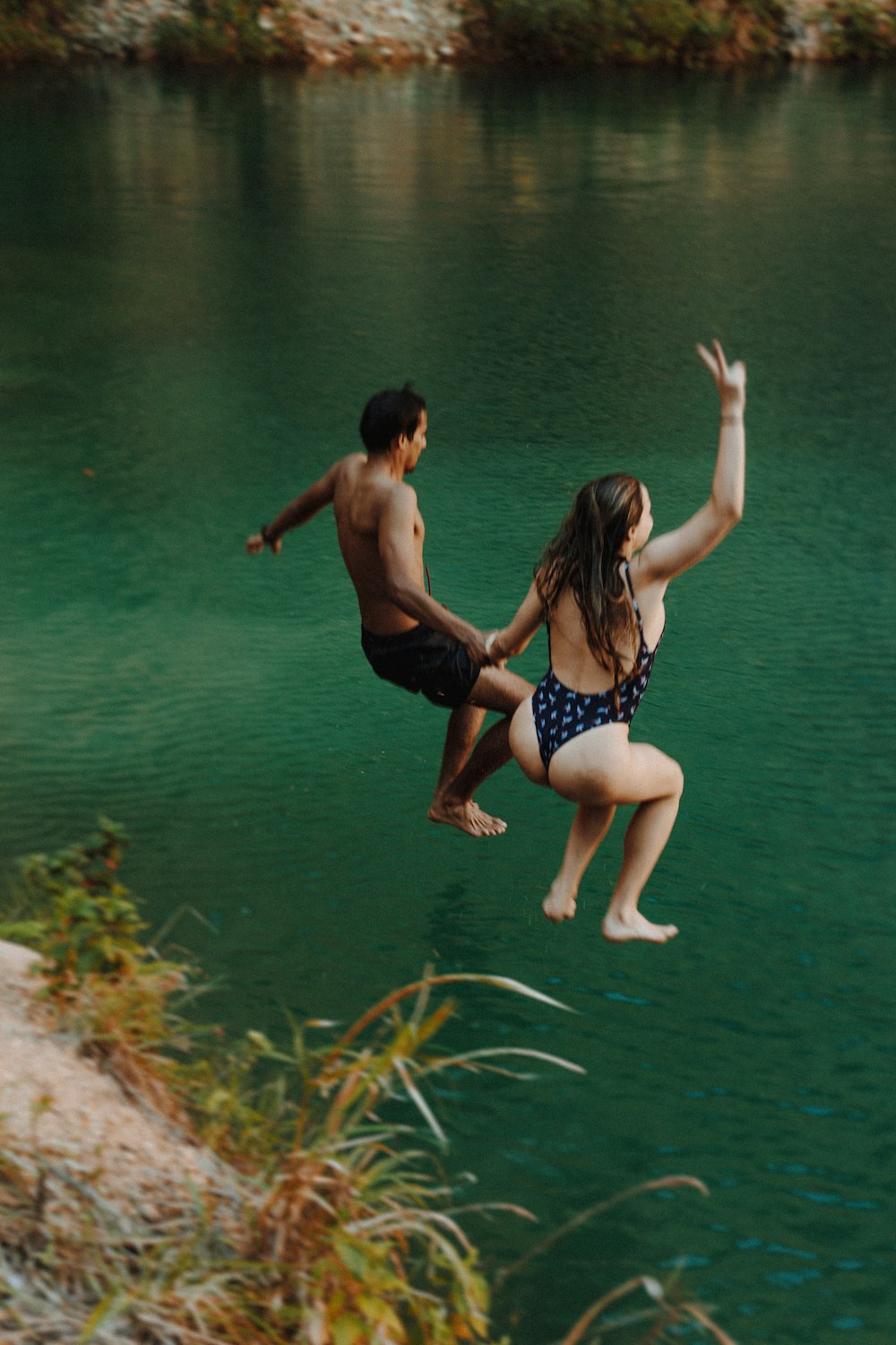 a man and woman jumping into a lake