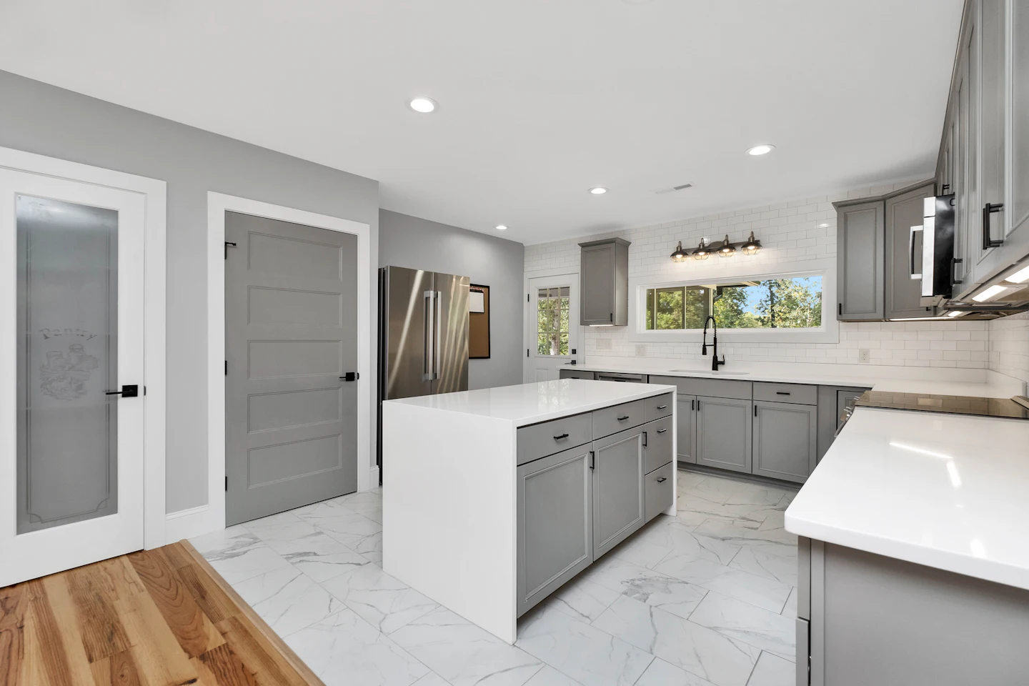Gray kitchen cabinets and an island with a white quartz top
