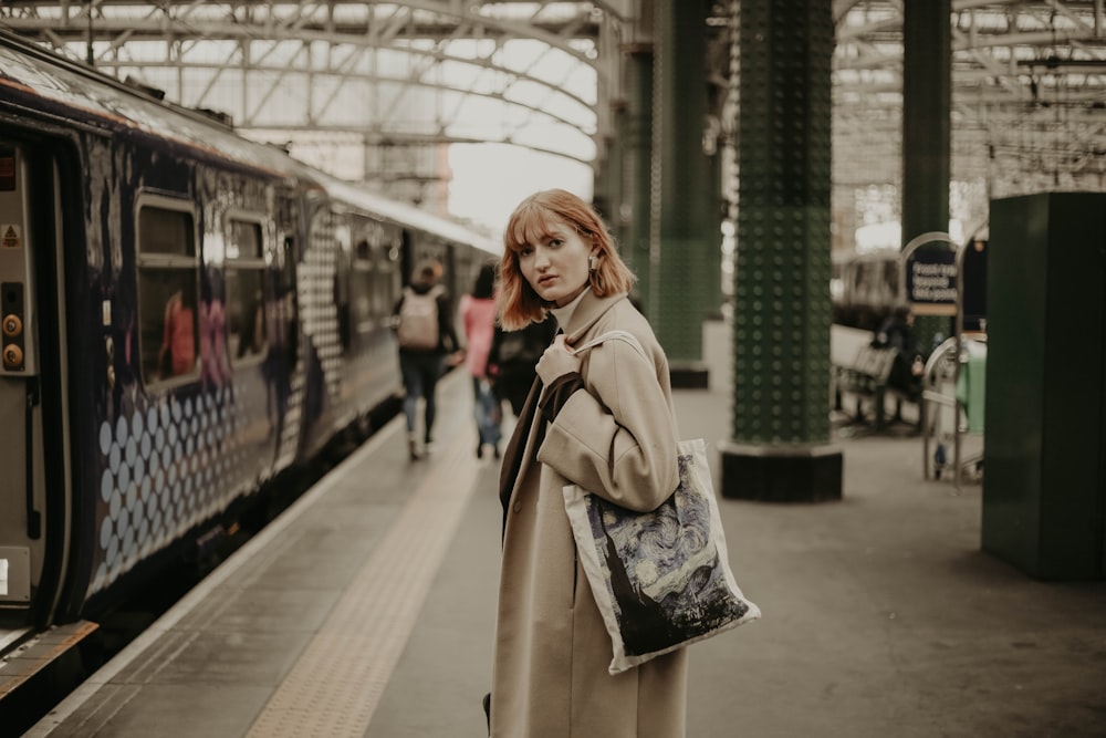 a woman in a trench coat standing next to a train